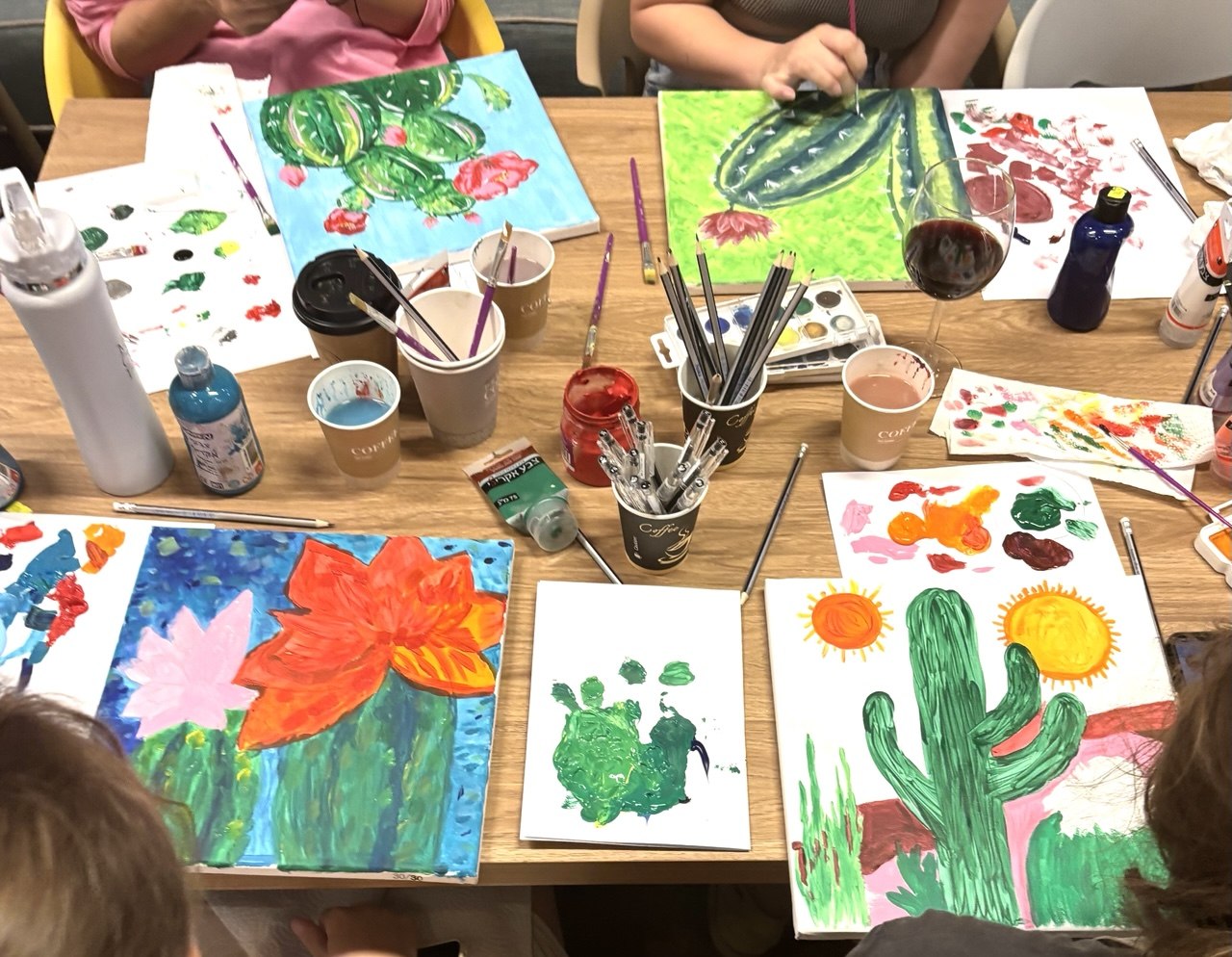 A class in progress - painted cacti and flowers, paints and brushes across the table