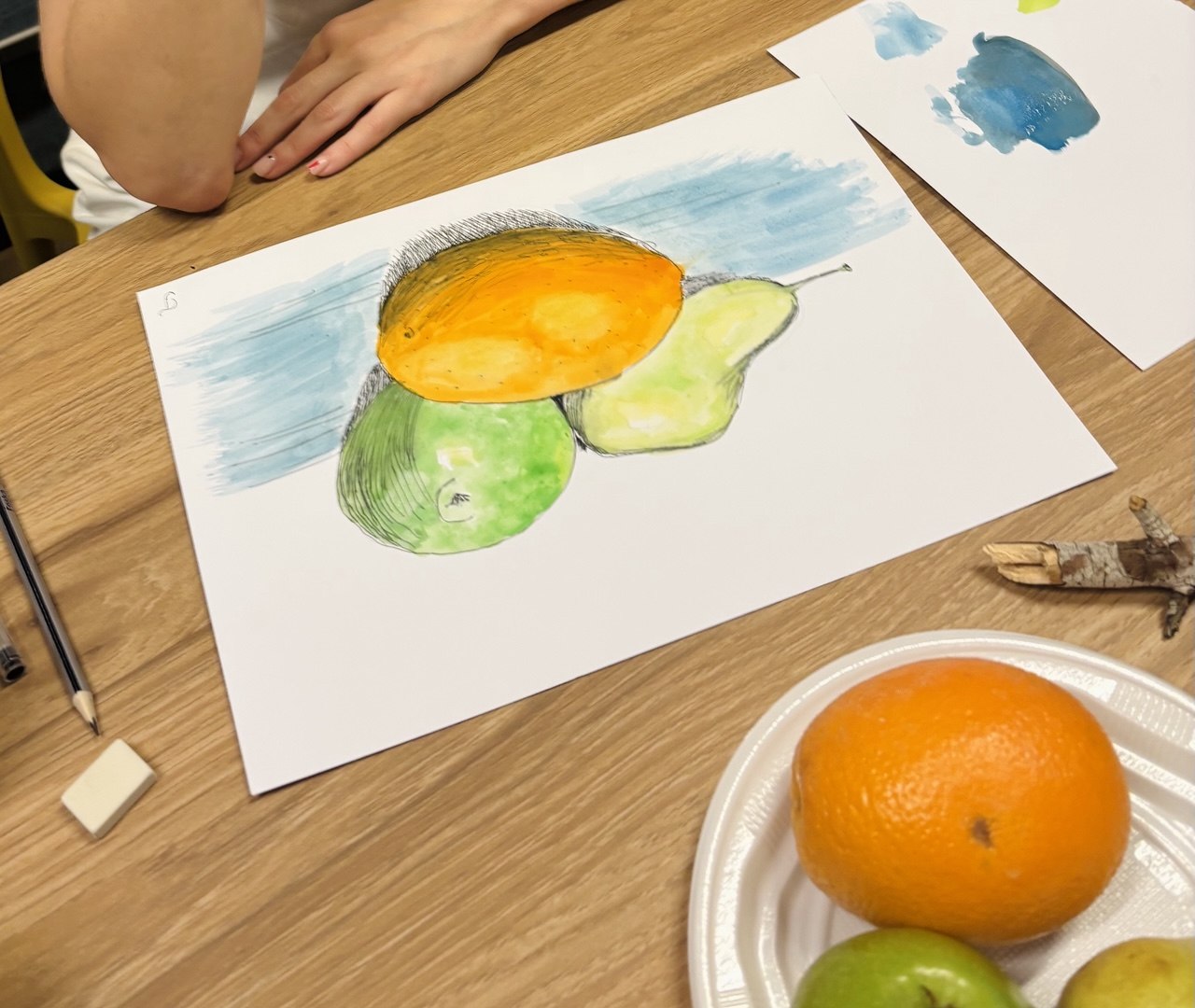 A student's watercolour still life of a mango, apple and pear, painted from the fruit on the table