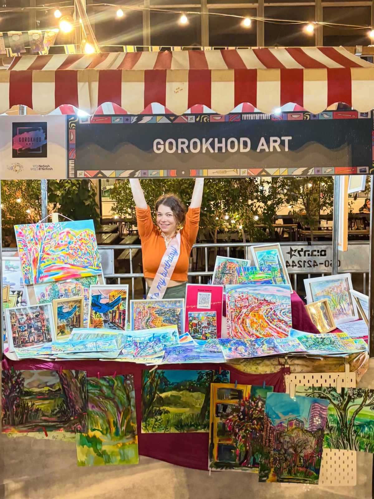 Inna at her Gorokhod Art market stall, paintings displayed around her